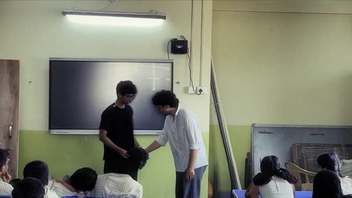 Two facilitators acting the Spot the Bullying skit at the front of the classroom, the class watching from their desks