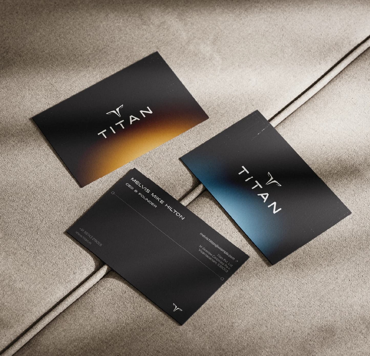 Three business cards fanned on linen — one amber, one blue, one showing the contact side